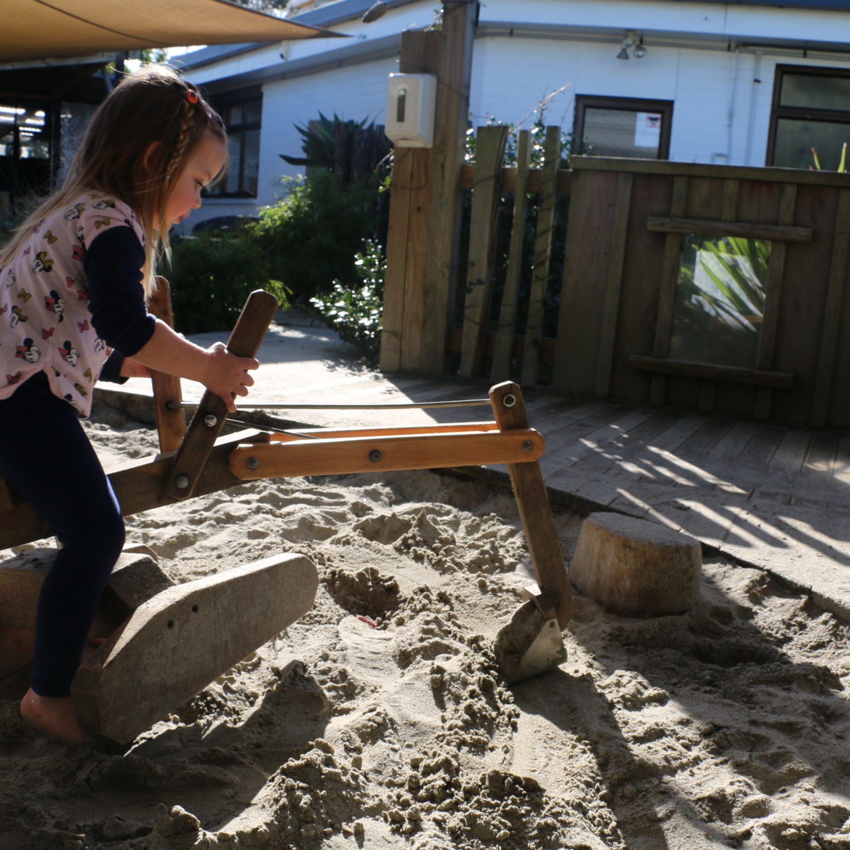 child playing on a wooden digger in a sandpit