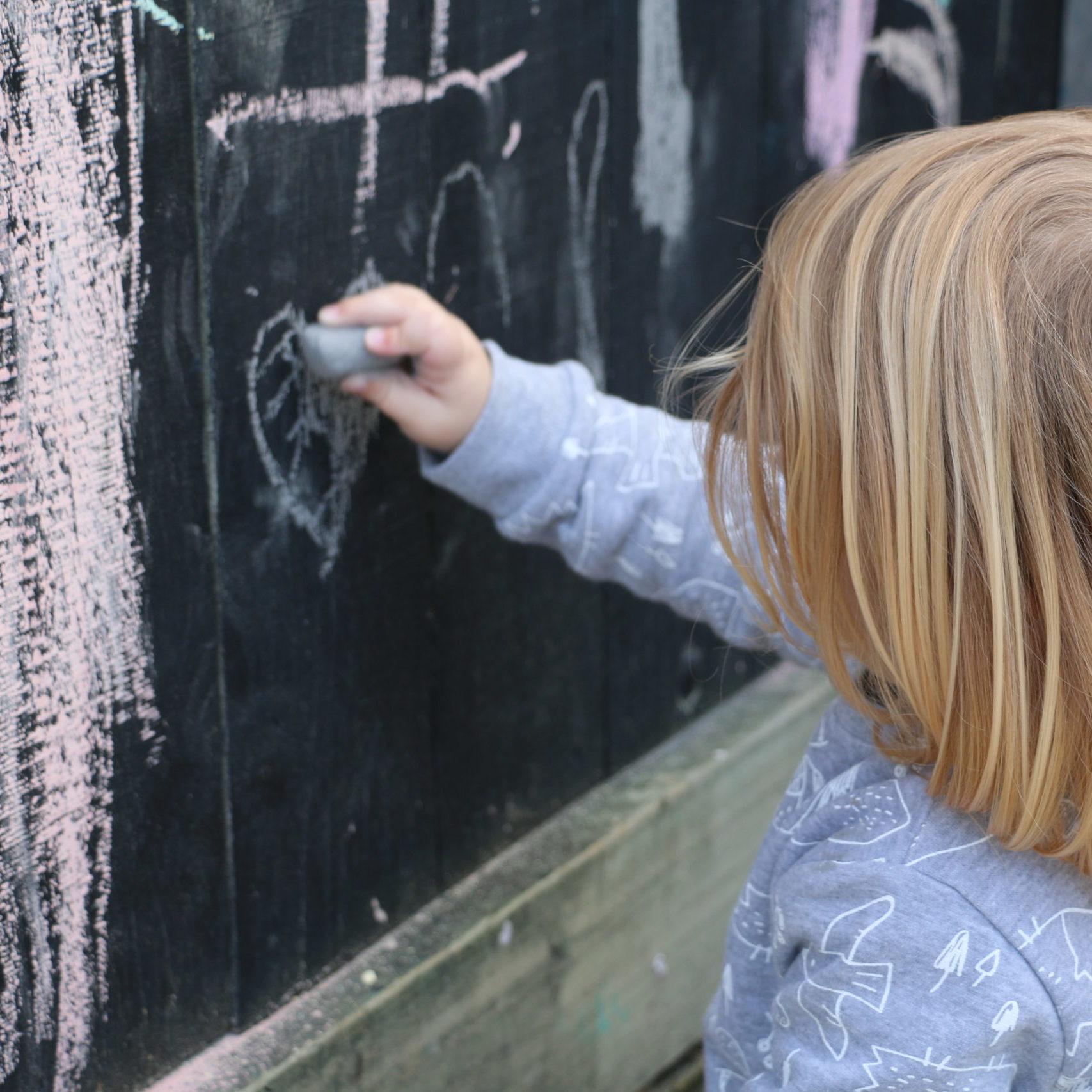 child drawing with chalk on black fence