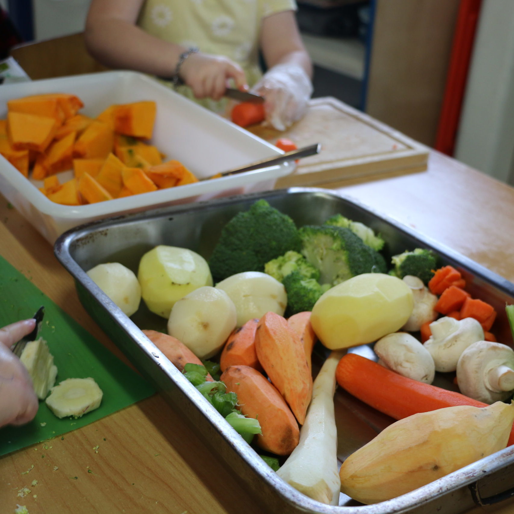 Tray of peeled vegetables and children cutting them
