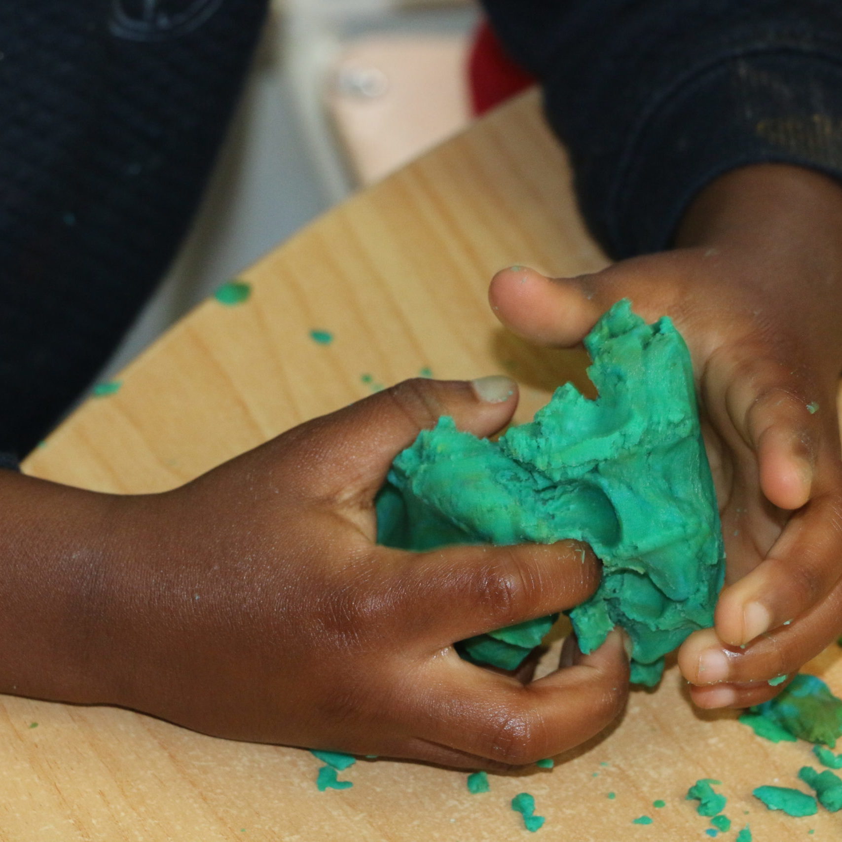 child's hands squeezing green playdough